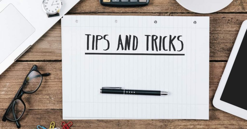 Office desk with electronic devices, computer and paper, wood table with the words “tips and tricks” on the notebook.