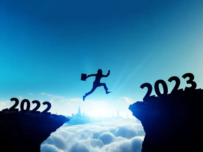 Businessman with briefcase jumping from 2022 cliff to 2023 cliff.
