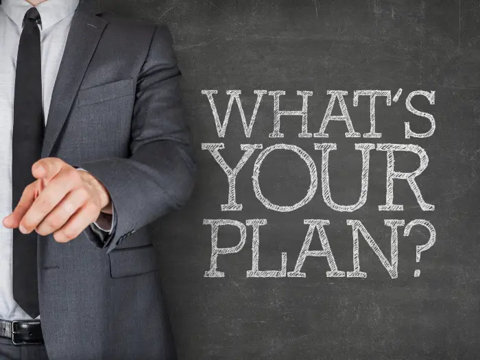 A man standing next to a blackboard with “Whats you plan” written on it