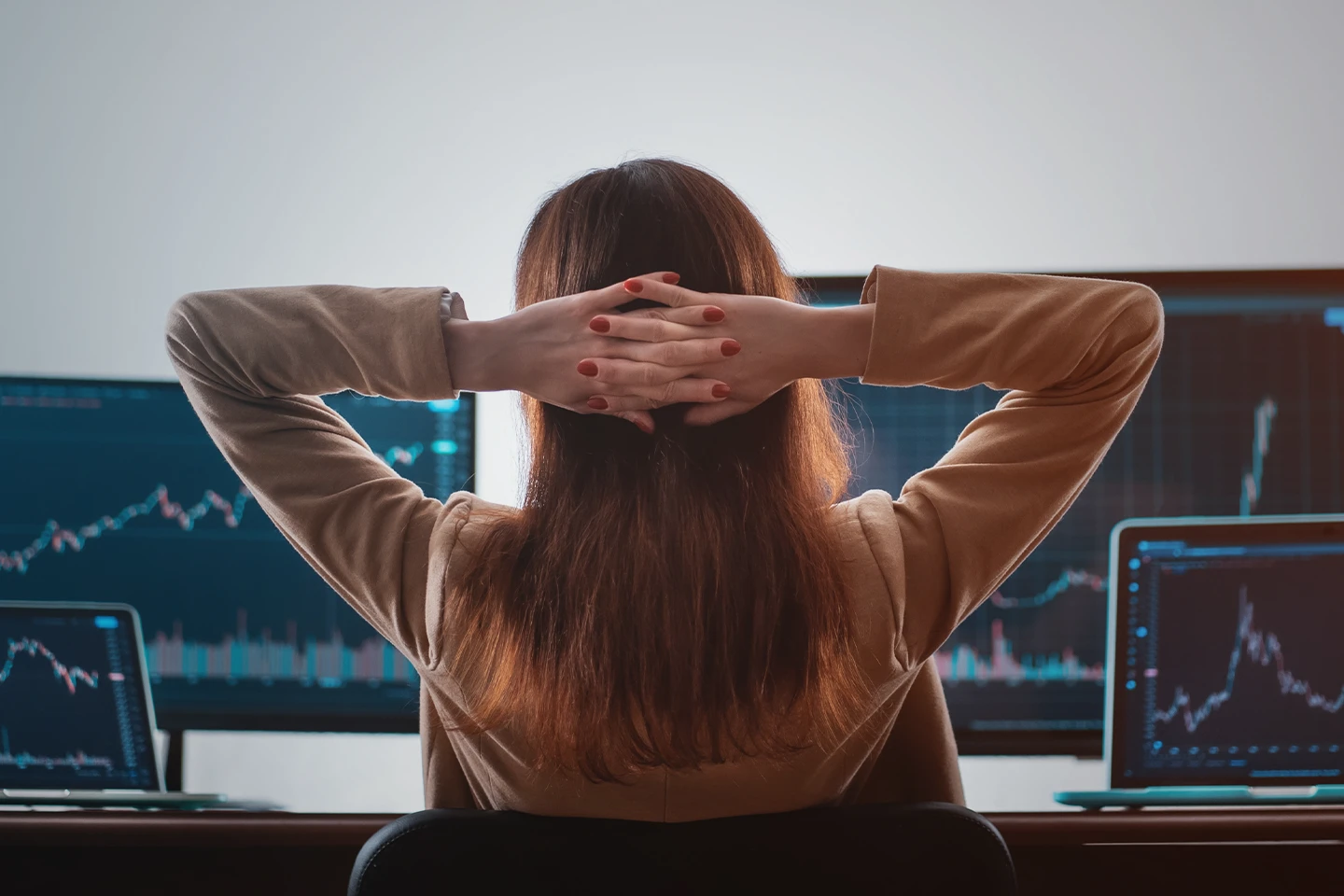 Trader leaning back in chair and reviewing financial market chart data across multiple monitors.