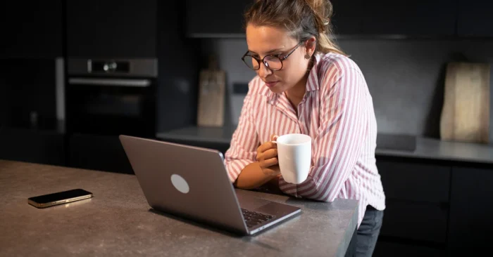 A focused woman prepares for the CFA exam through self-study, using a laptop and study materials in a quiet home setting