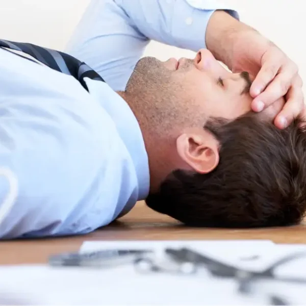 Stressed man in business attire lying on the floor with hand on forehead, surrounded by office documents and a coffee cup-illustrating burnout while studying for the CFA Level 1 exam.