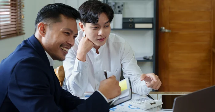 Two CFA Level 1 candidates discussing practice MCQs and study strategy using printed question sets and data charts.