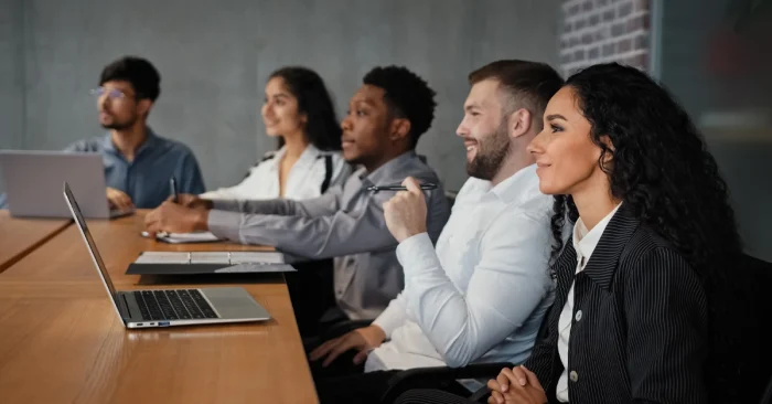 A group of CFA Level 1 candidates following the best CFA Level 1 mastery guide, complete with a study plan and mock exams, using laptops and notes in class.